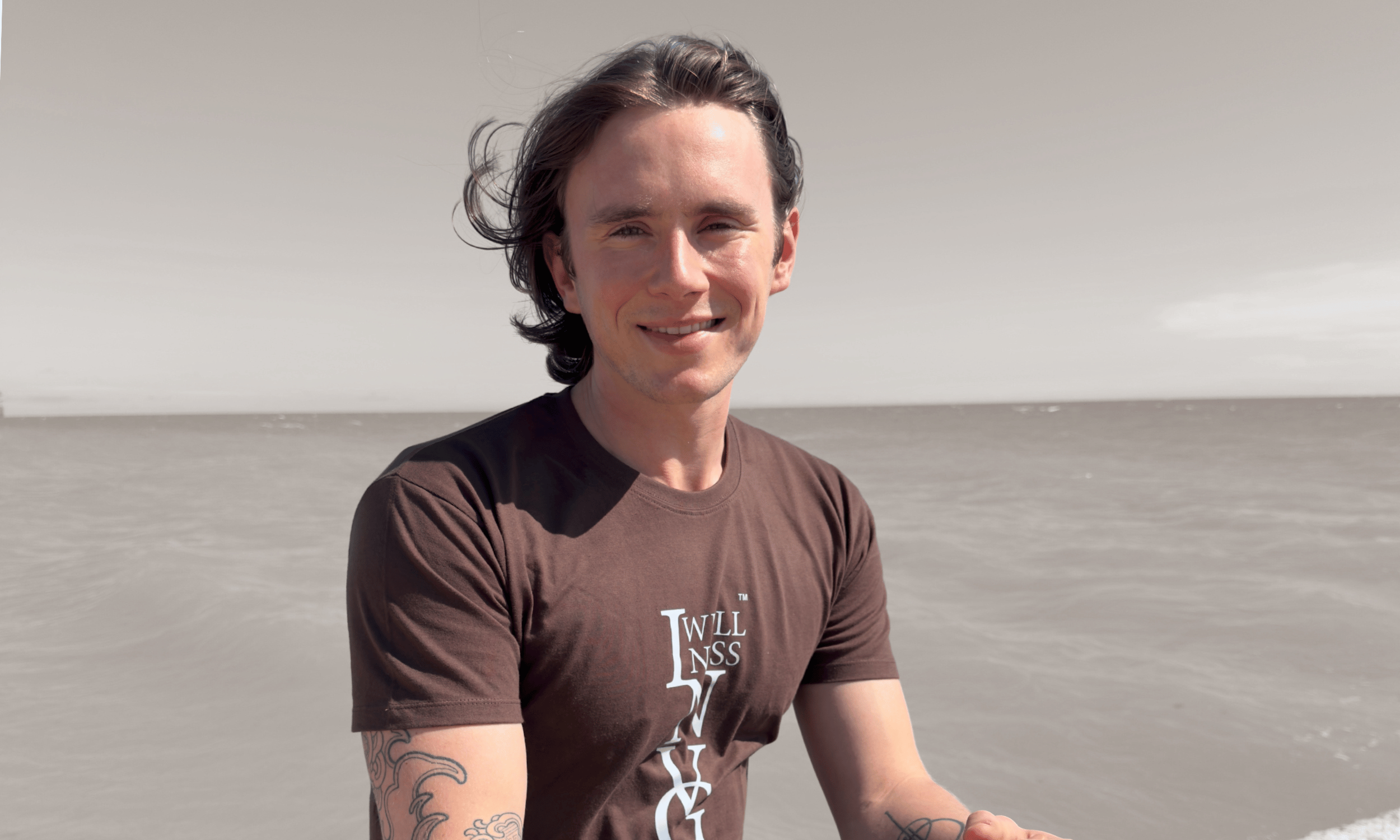 Man wearing a brown t-shirt with text, standing against a plain background