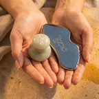 Two hands holding a jade roller and a blue facial massager on a textured surface.