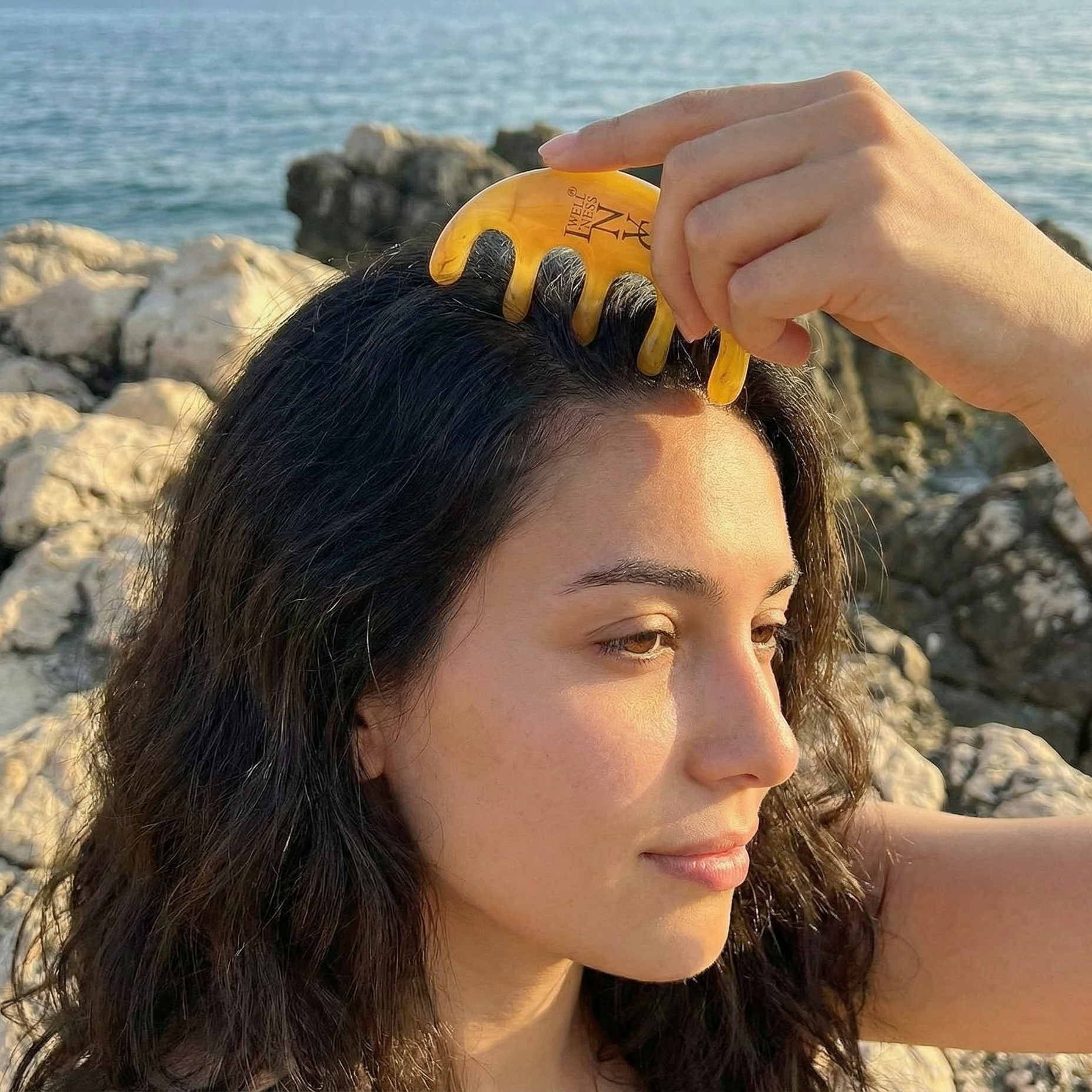 Woman combing her hair with a yellow comb by the ocean.