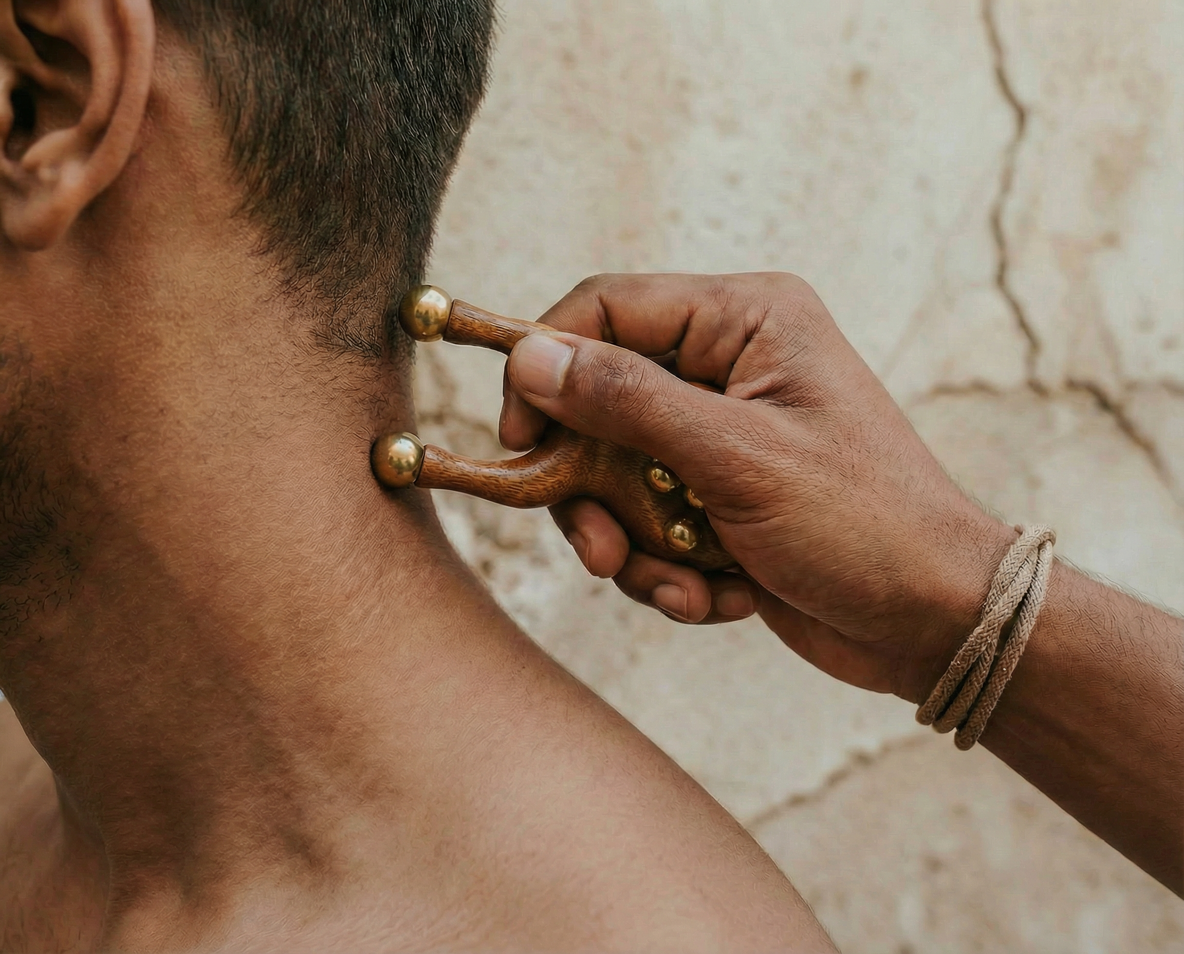 Hand using a wooden tool on a person's neck against a textured wall background